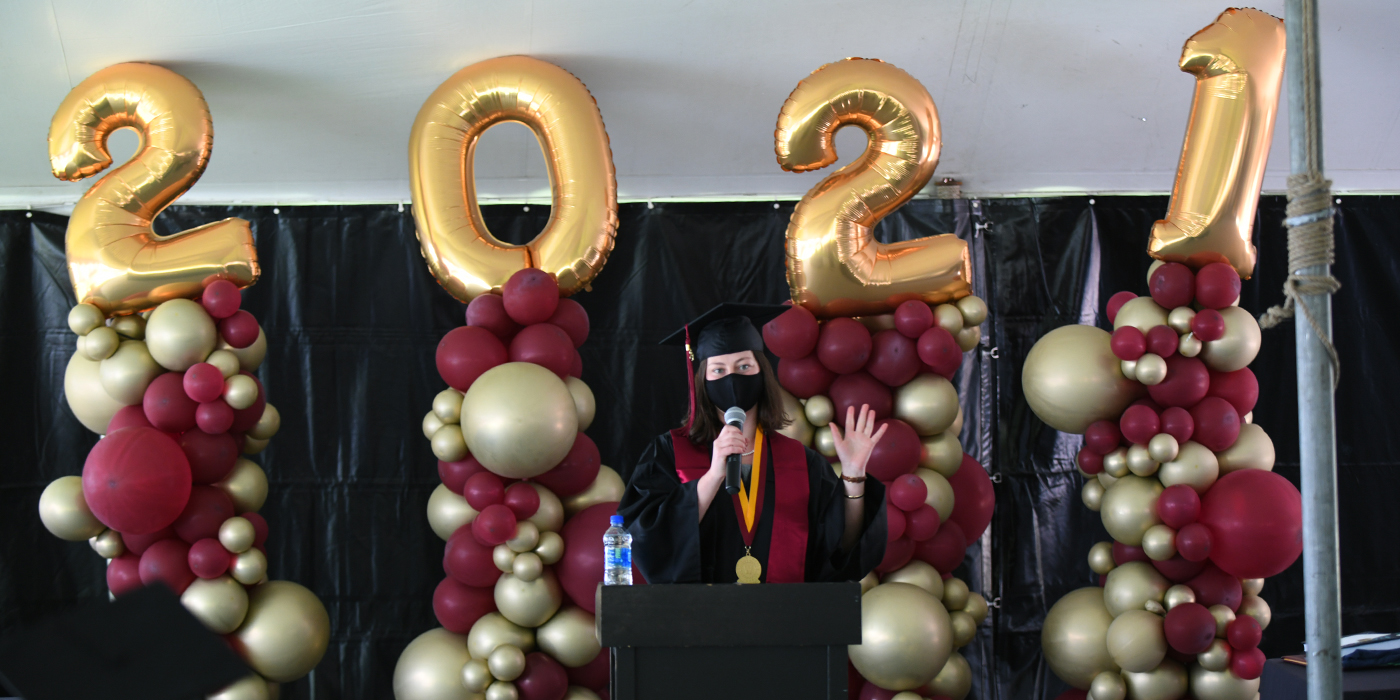 a student speaks at a podium in front of large 2021 balloons