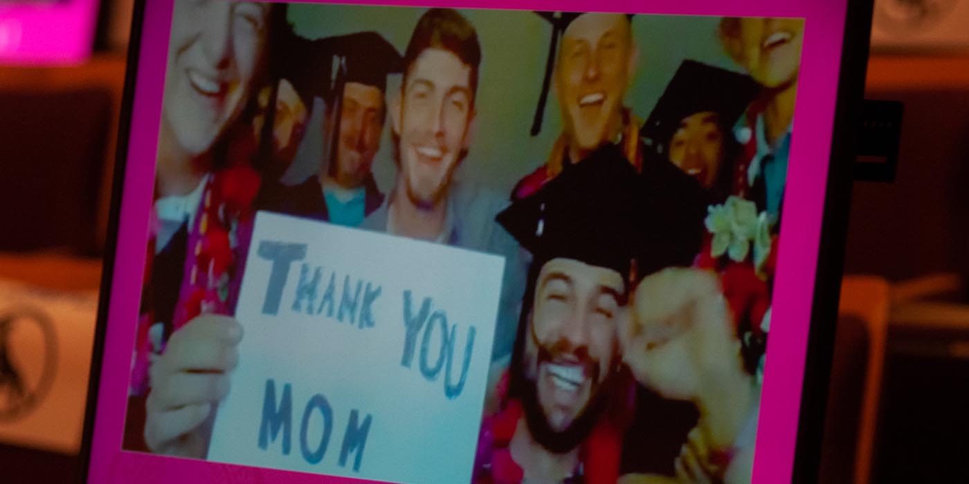 A group of graduates on the computer screen with a "thank you mom" sign