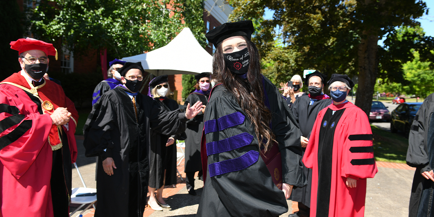 a masked law graduate stands distanced from a group of faculty outside diploma in hand