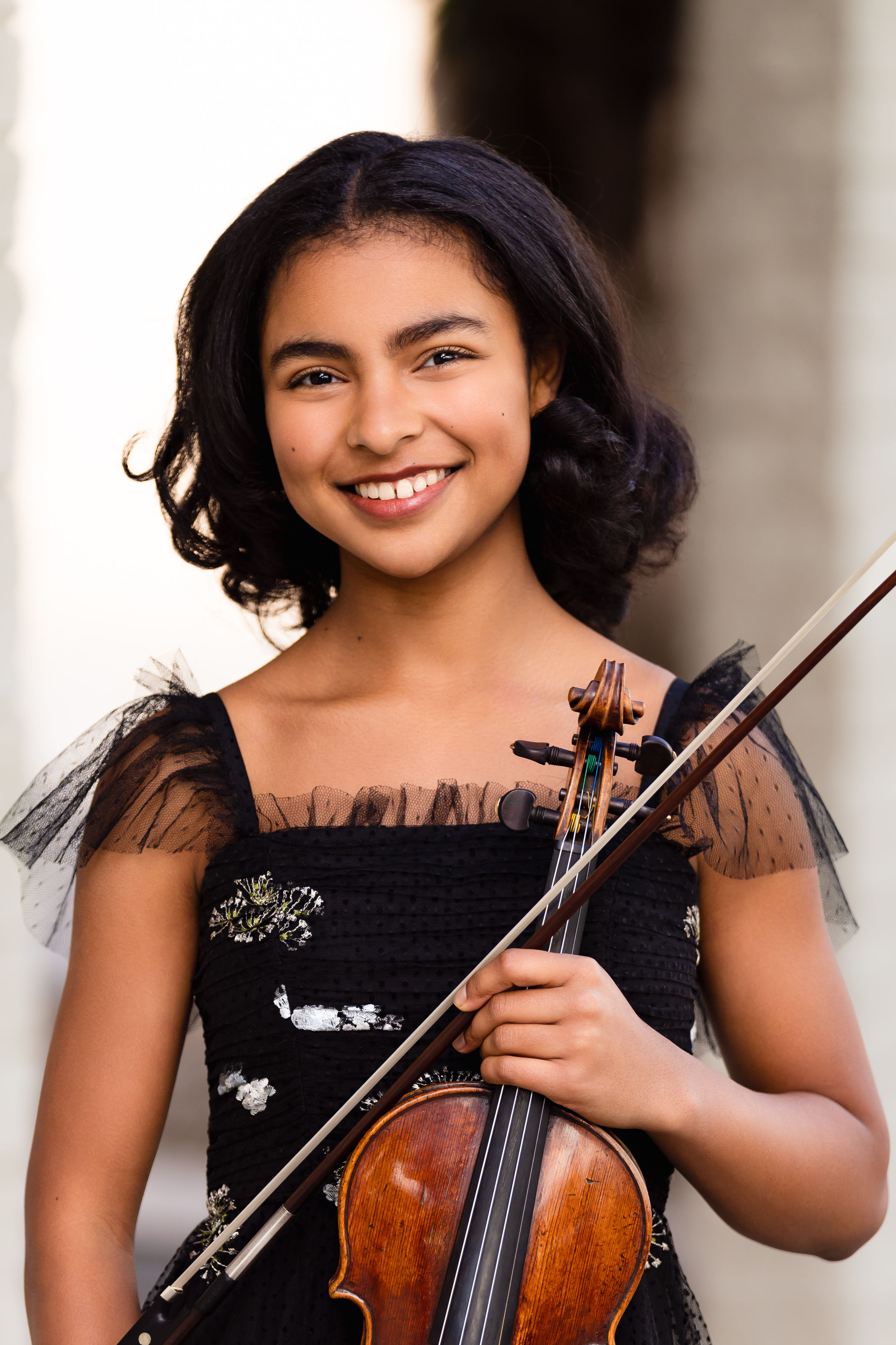 Young woman smiling in a black dress holding her violin