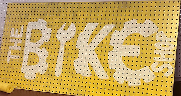 Painted Bike Shop sign on yellow pegboard